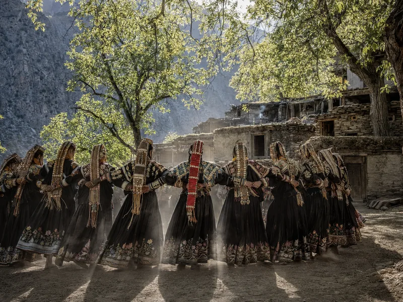 Traditional Kalash timber and stone houses stacked up a steep green valley side among walnut trees in Bumburet, Chitral.
