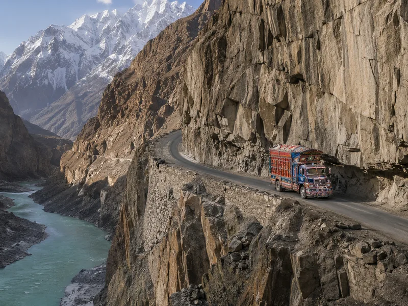 A hand-painted Pakistani cargo truck on the Karakoram Highway where it is cut into a cliff high above the turquoise Hunza river.