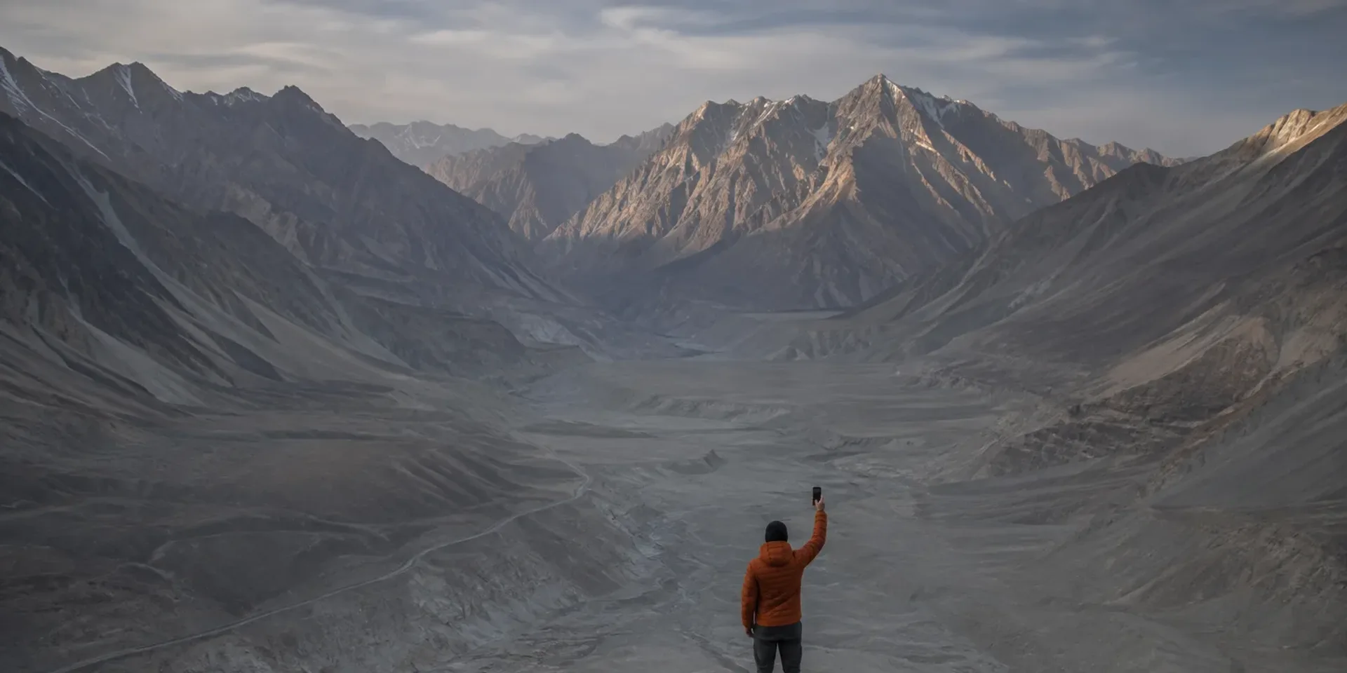 A hand holding a phone up against an enormous empty Karakoram valley, searching for a signal.