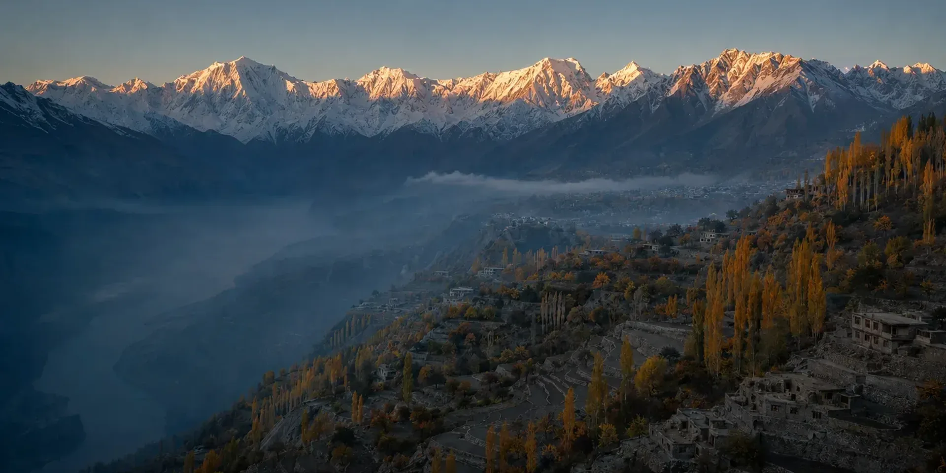 The Hunza valley from Duikar at sunrise in late October: the whole Karakoram wall lit along the skyline, golden poplars on the terraces below, mist lying along the river.