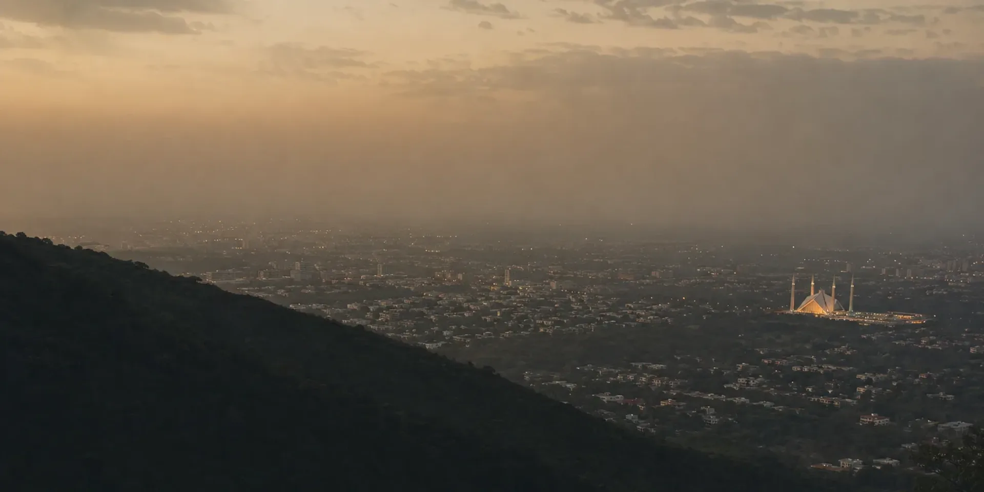 Islamabad from the Margalla Hills at dusk, the wooded ridge falling away to the green city below.