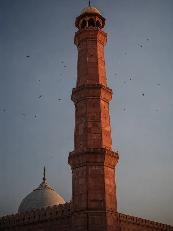 A minaret of the Badshahi Mosque rising against a deepening sky in warm late-afternoon light.