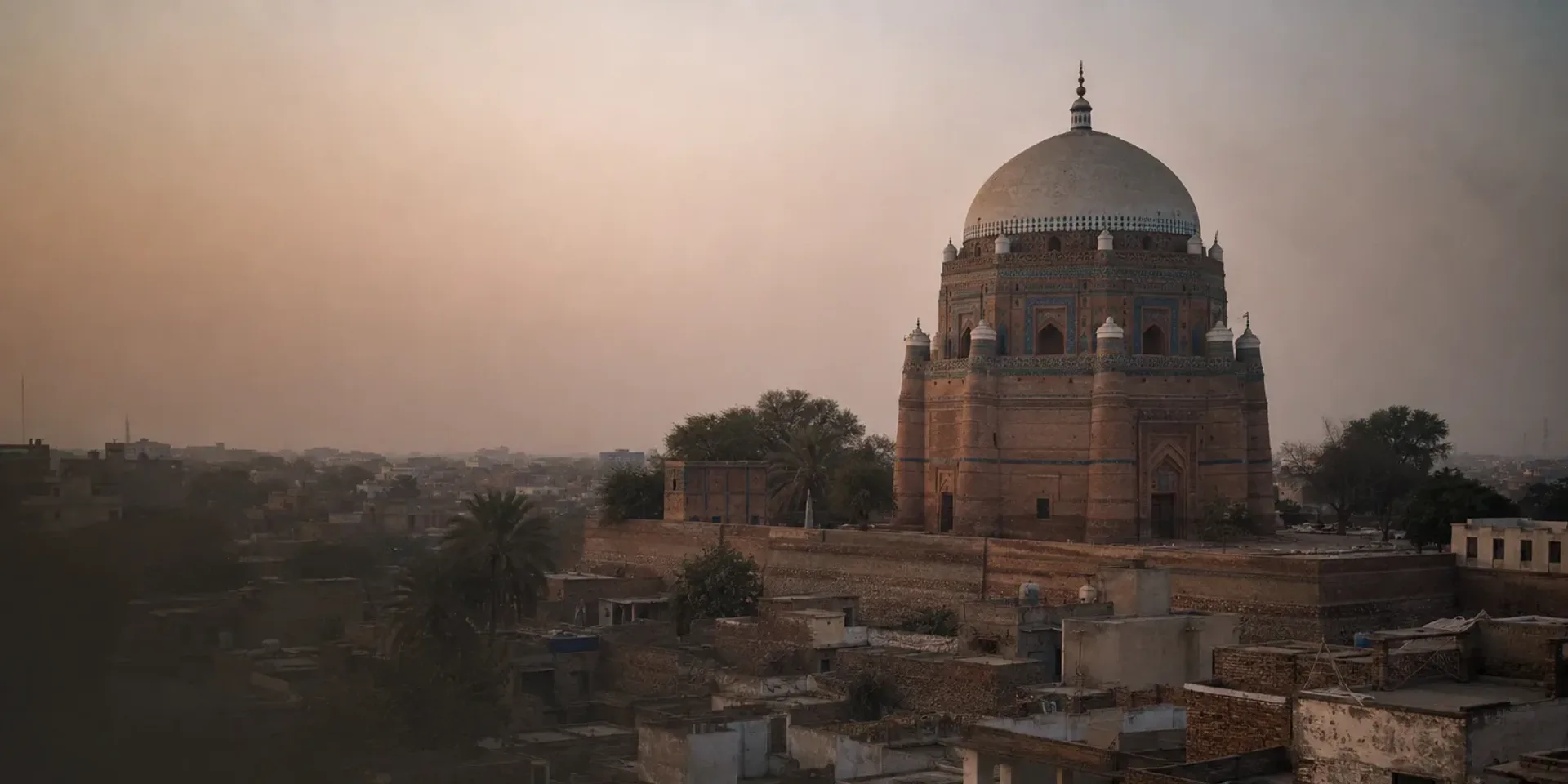 Multan's old city at dusk, the tiled dome of Shah Rukn-e-Alam standing on its mound above flat rooftops.