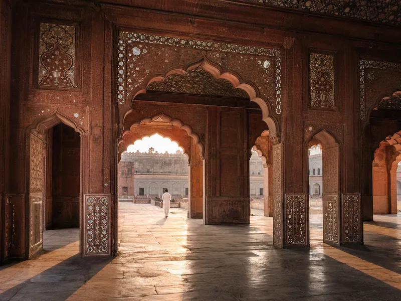Red sandstone Mughal arches inlaid with white marble at Lahore Fort, deep shadow under the arcade opening onto a sunlit courtyard.