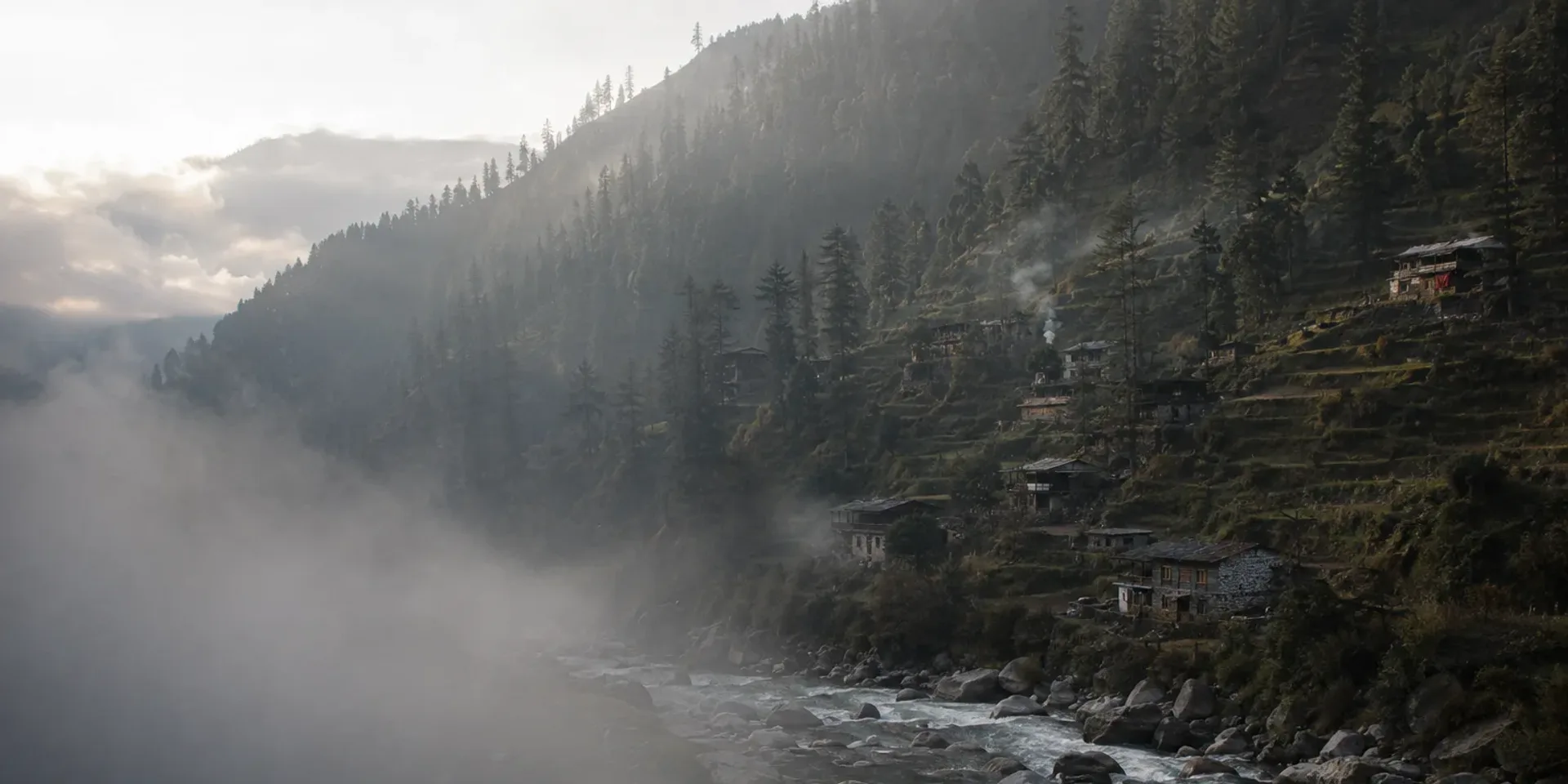 The upper Swat valley in the morning, the river running over pale boulders below forested slopes and wooden houses.