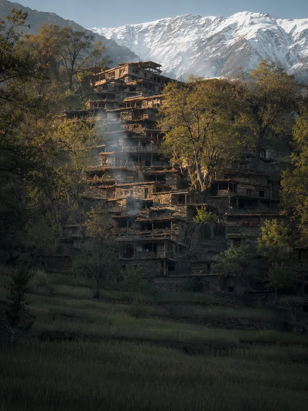 Kalash timber and stone houses stacked up a steep valley side in Bumburet, each flat roof the terrace of the house above.