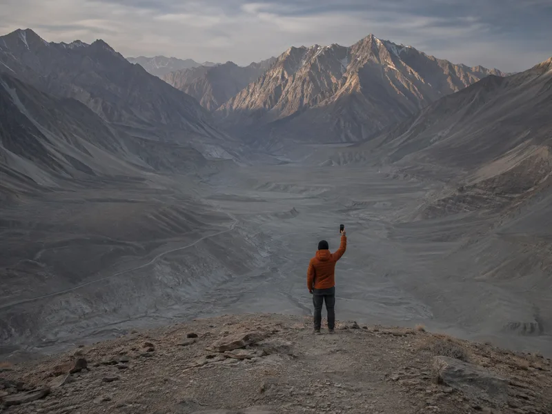 A hand holding a phone up against an enormous empty Karakoram valley, searching for a signal.