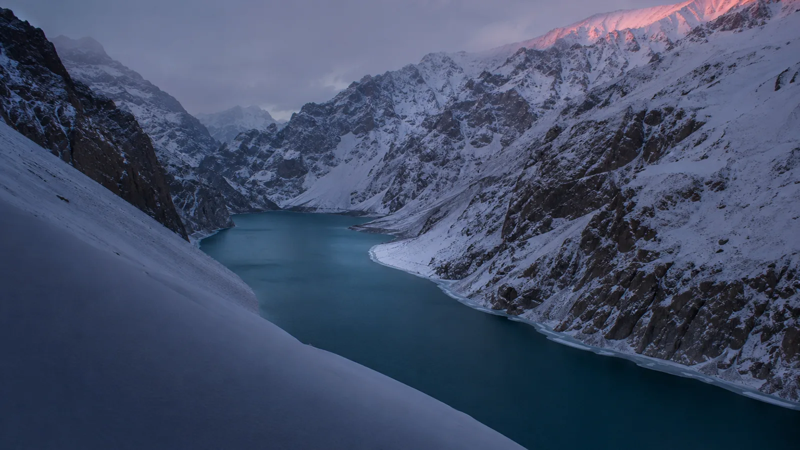 Attabad Lake in Upper Hunza in winter, deep turquoise water between snow-covered mountain walls.