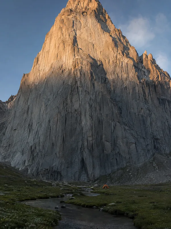 The granite face of Amin Brakk rising above the green meadow of Mingulu Broq in Nangma Valley, a single tent tiny below it.