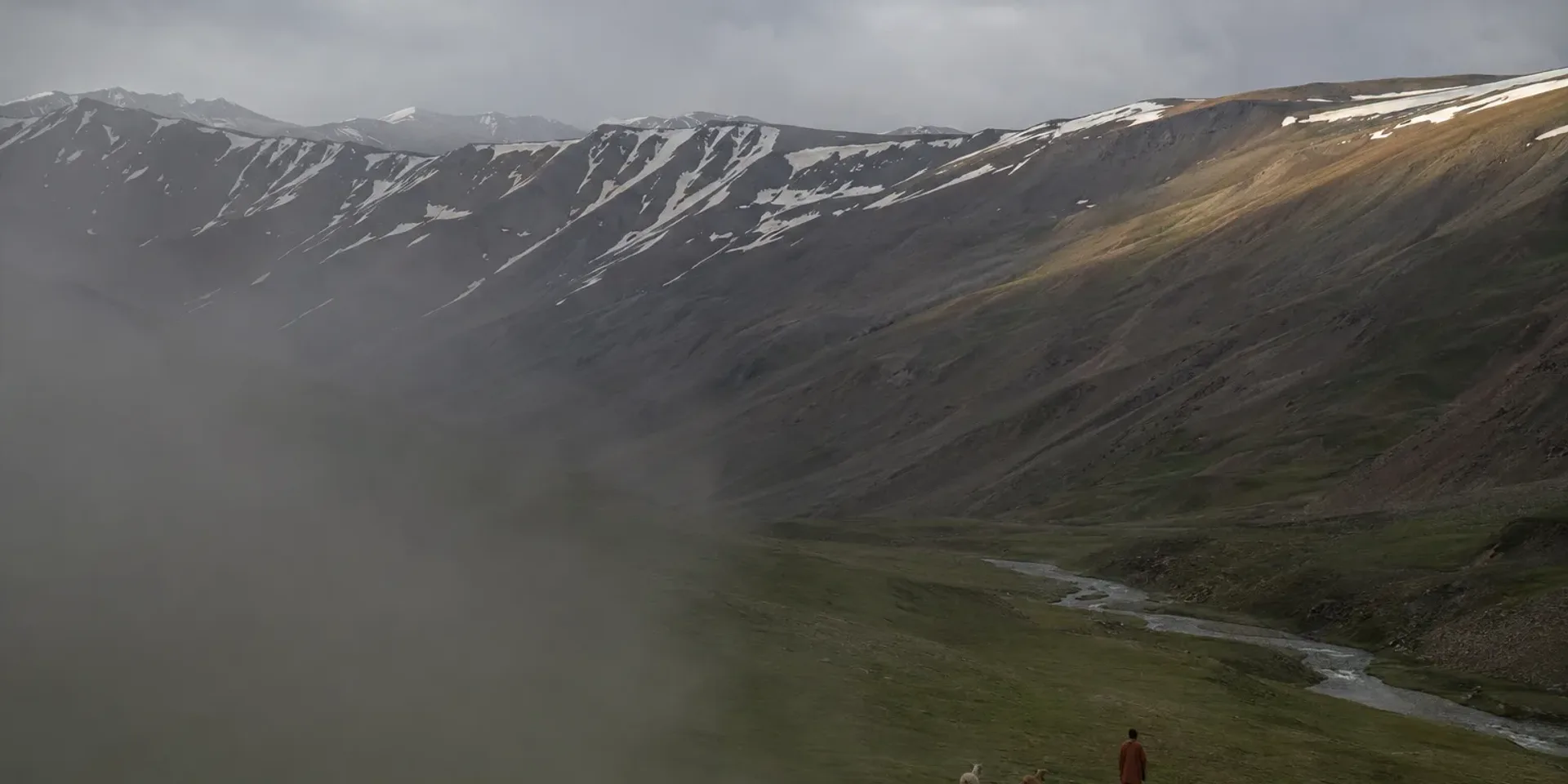 The Kaghan valley in late summer, green pasture and river below bare slopes rising to a snow-streaked ridge.